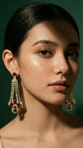 Gold chandelier earrings adorned with red gemstones and clear crystals, worn by a woman with sleek dark hair.