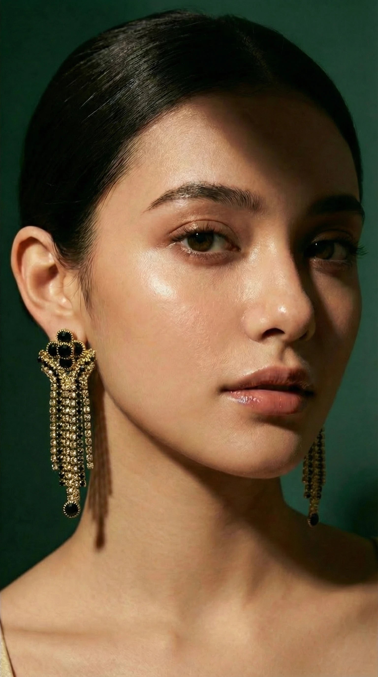 Gold and black beaded long dangle earrings worn by a woman with sleek dark hair.