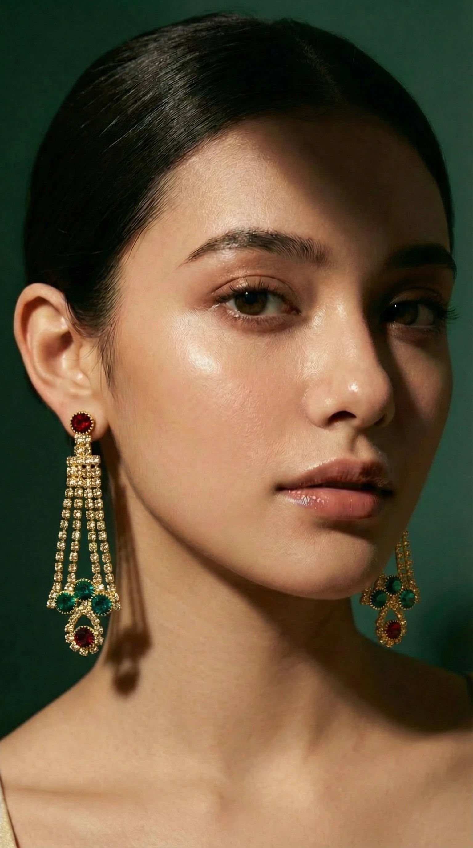 Gold chandelier earrings featuring red and green gemstones with multiple rows of small sparkling stones hanging in a teardrop shape.