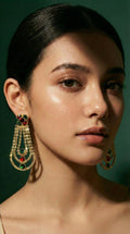 Gold chandelier earrings featuring red and green gemstones with multiple rows of small sparkling stones hanging in a teardrop shape.