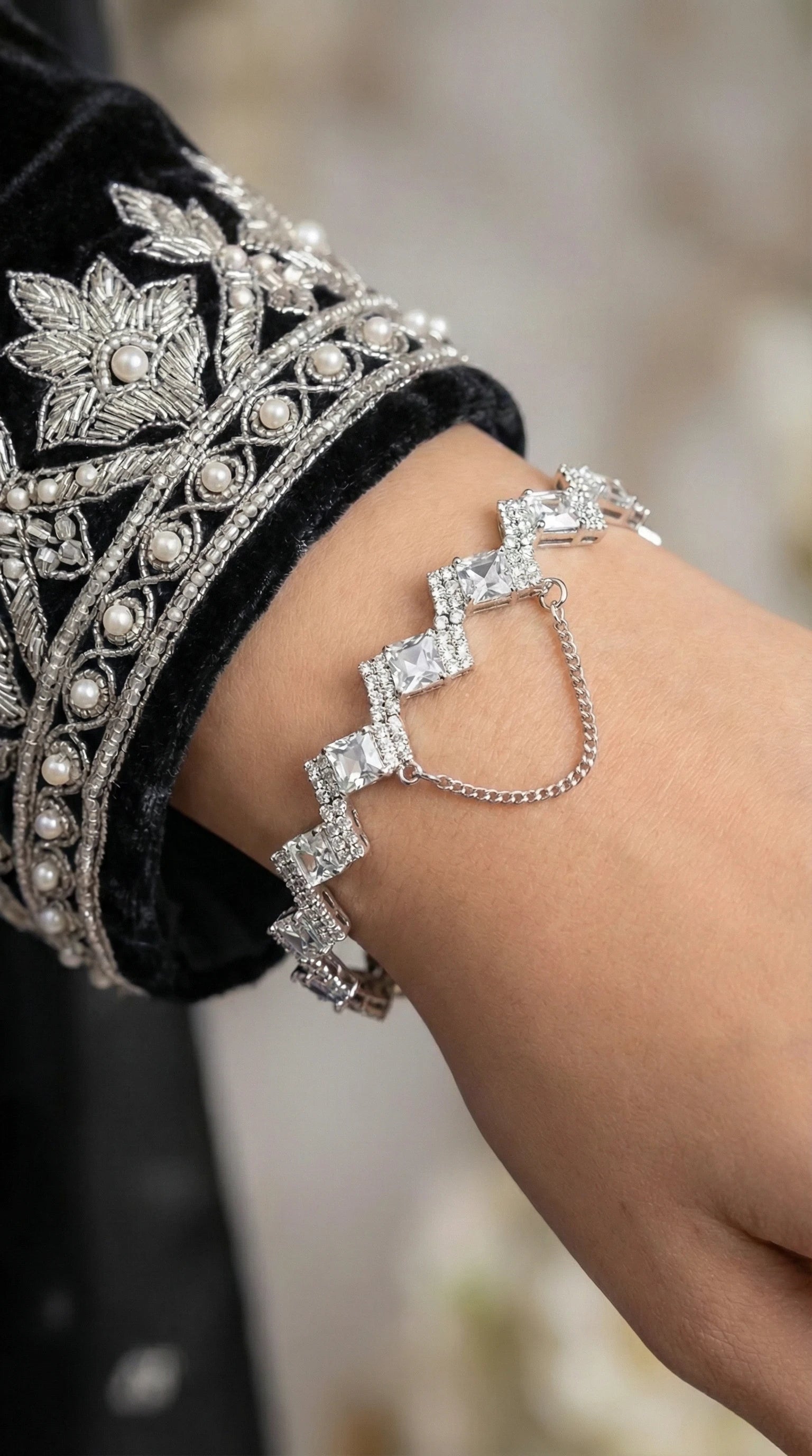 Silver bracelet with alternating square and round clear gemstones arranged in a zigzag pattern, worn on a wrist.