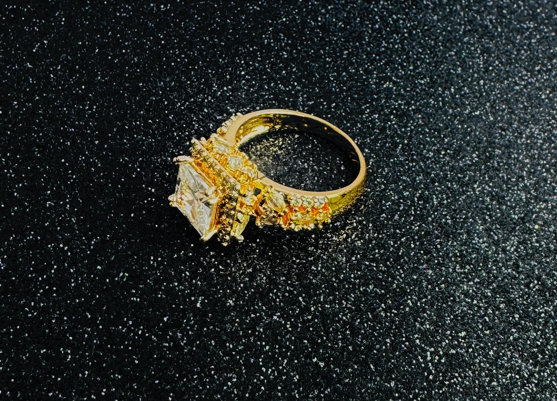 Gold ring with a large square-cut central gemstone and multiple smaller round diamonds set around the band in a layered design