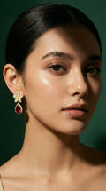 Gold floral-shaped earrings with small clear gemstones and a large teardrop-shaped red gemstone pendant.