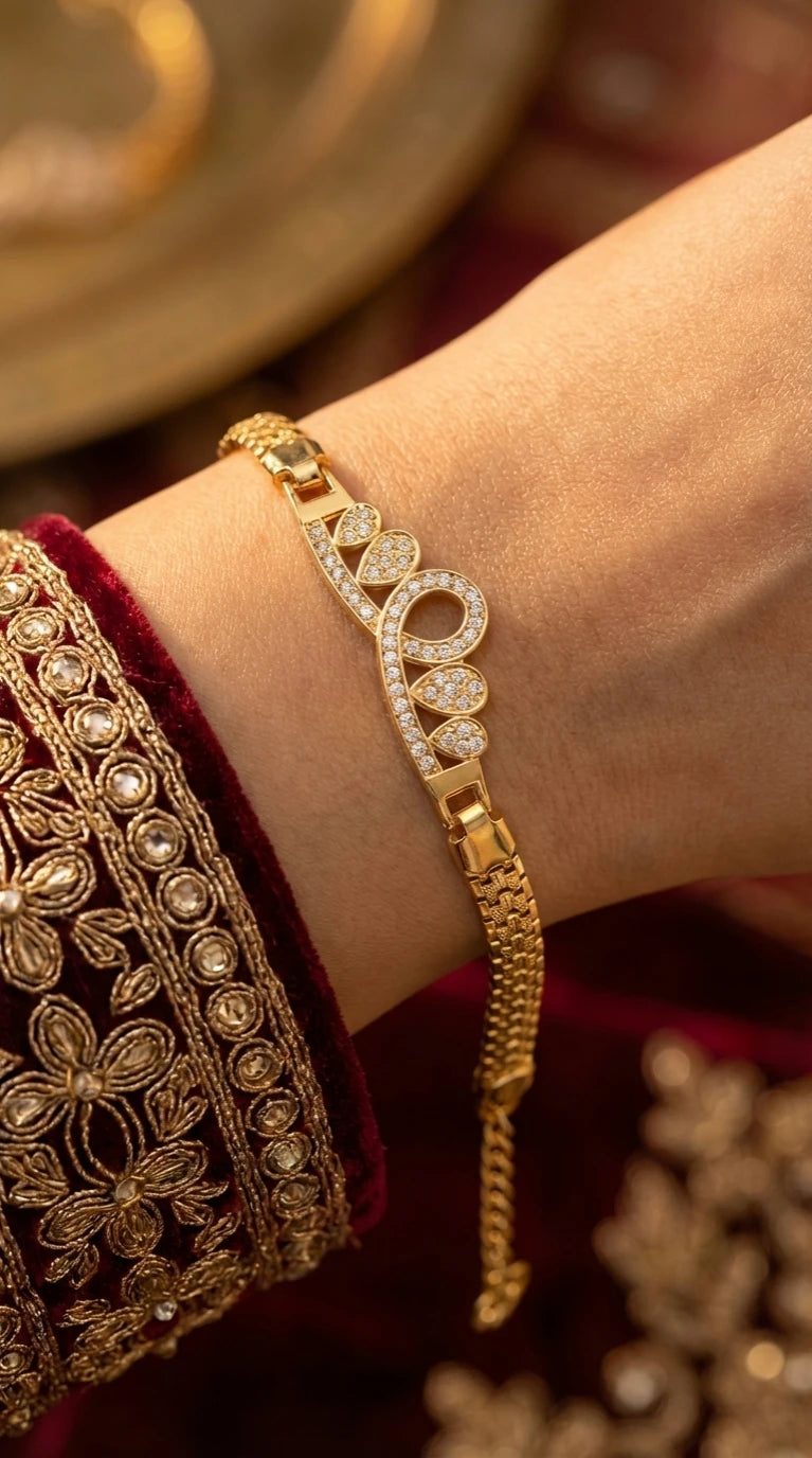 Gold bracelet with a crown lightning bolt design encrusted with clear gemstones, worn on a wrist with green embroidered fabric.