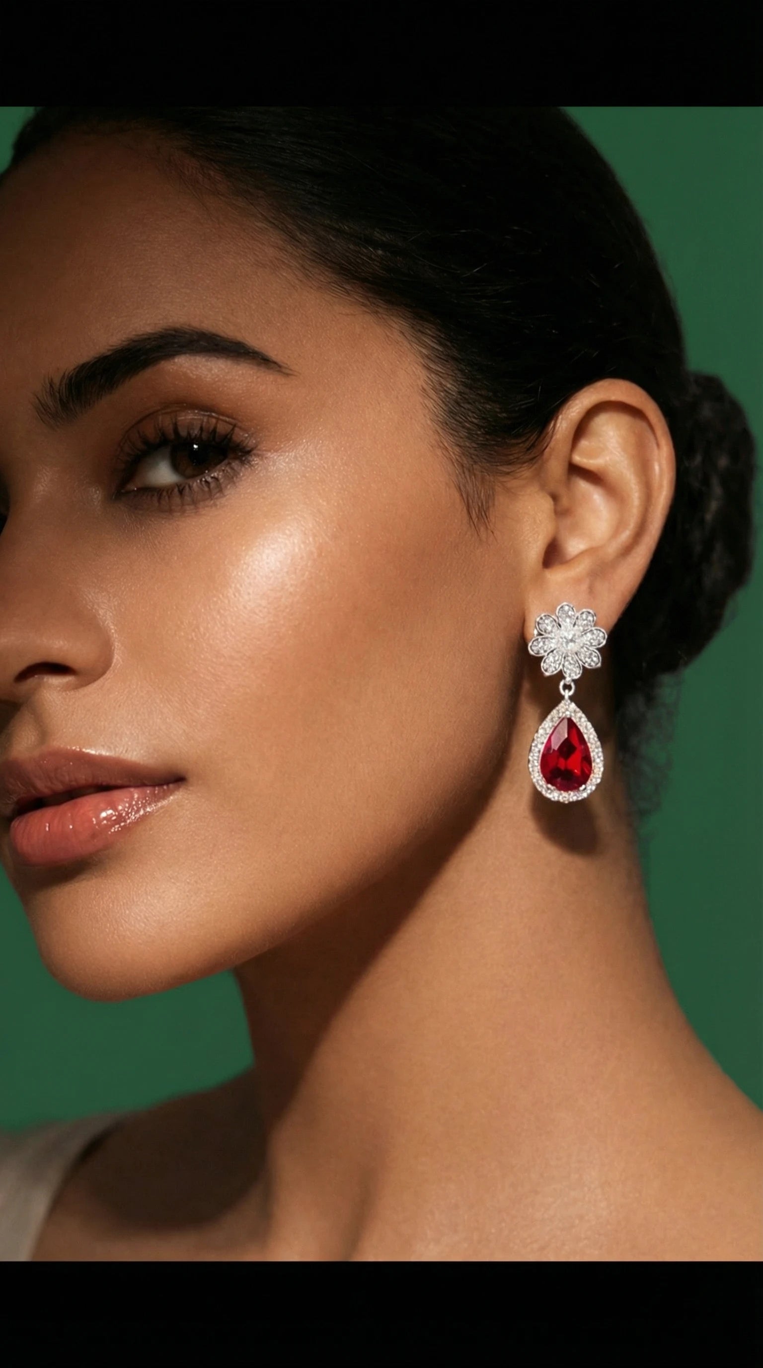 Gold floral drop earrings with small clear gemstones and a large teardrop-shaped red gemstone, worn by a woman.