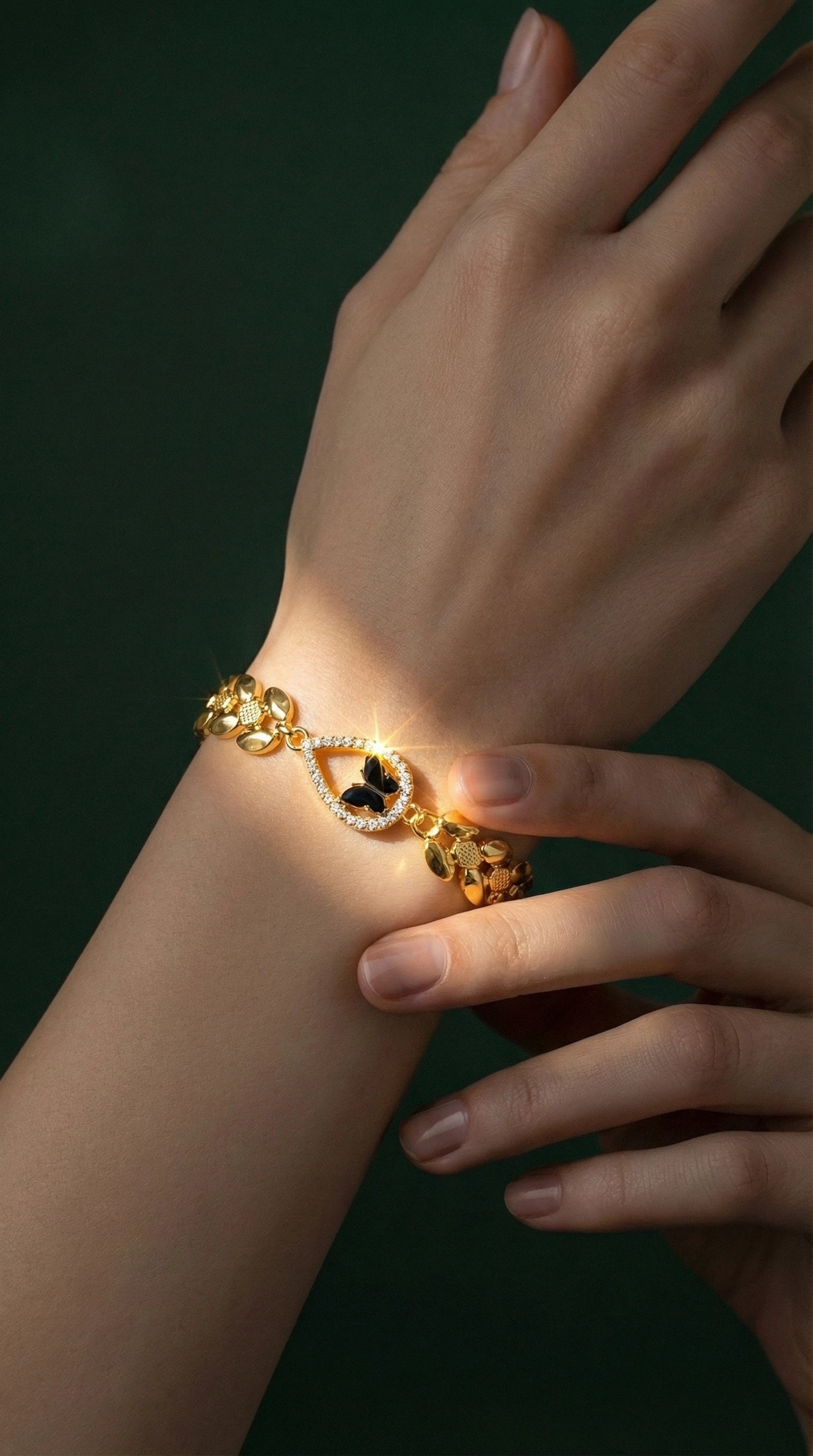Gold bracelet with a teardrop-shaped centerpiece featuring a black butterfly design surrounded by small clear gemstones, worn on a wrist.