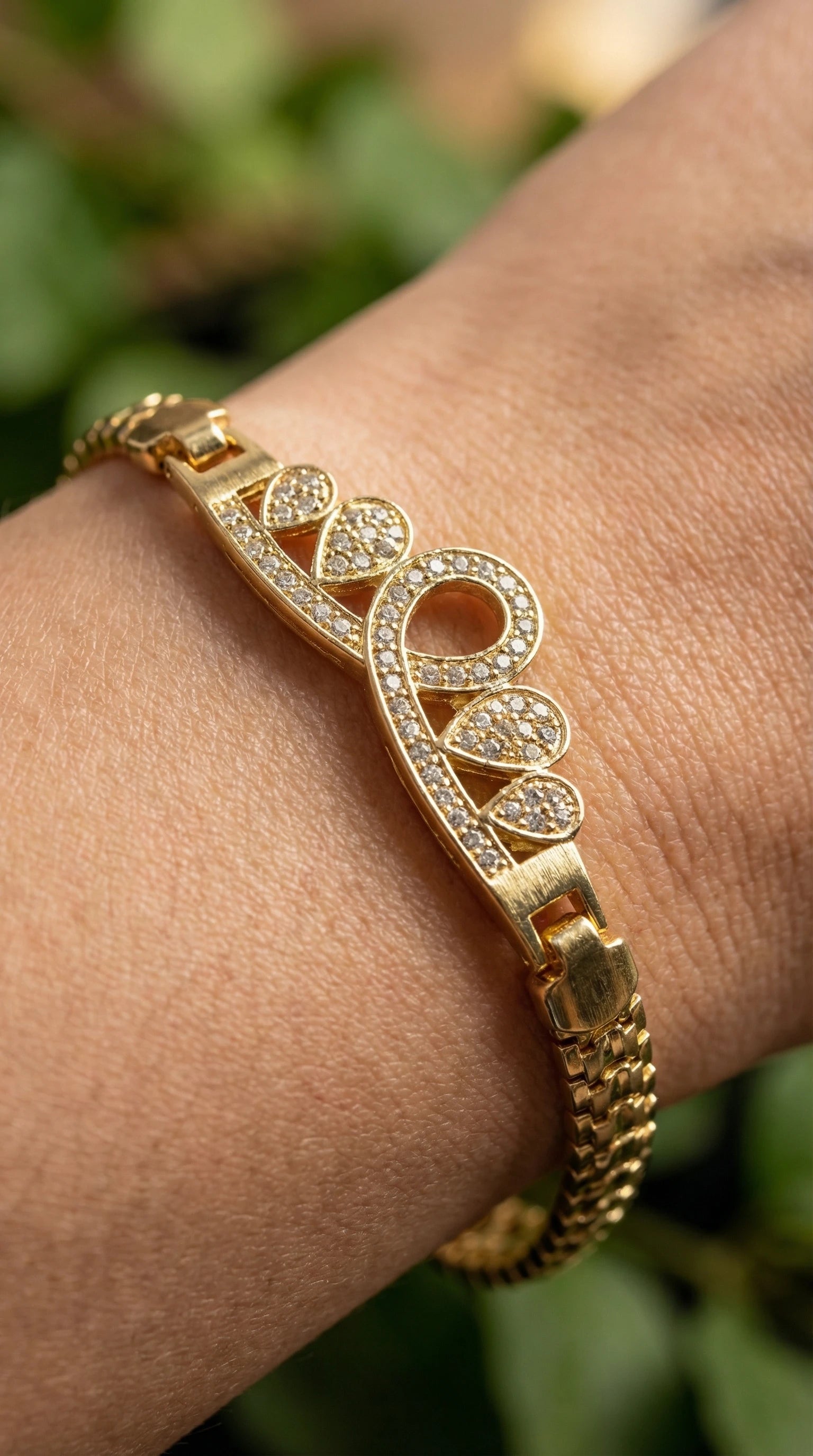 Gold bracelet with a crown lightning bolt design encrusted with clear gemstones, worn on a wrist with green embroidered fabric.