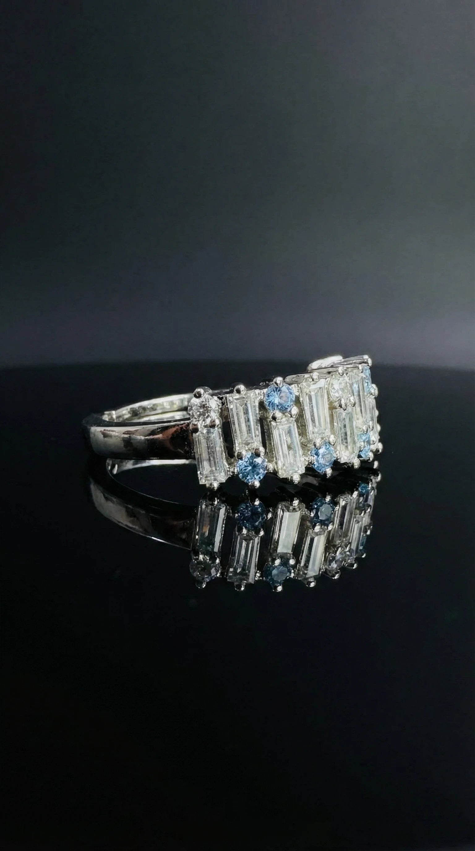 Silver ring alternating round blue gemstones and tapered baguette clear stones set in a continuous band