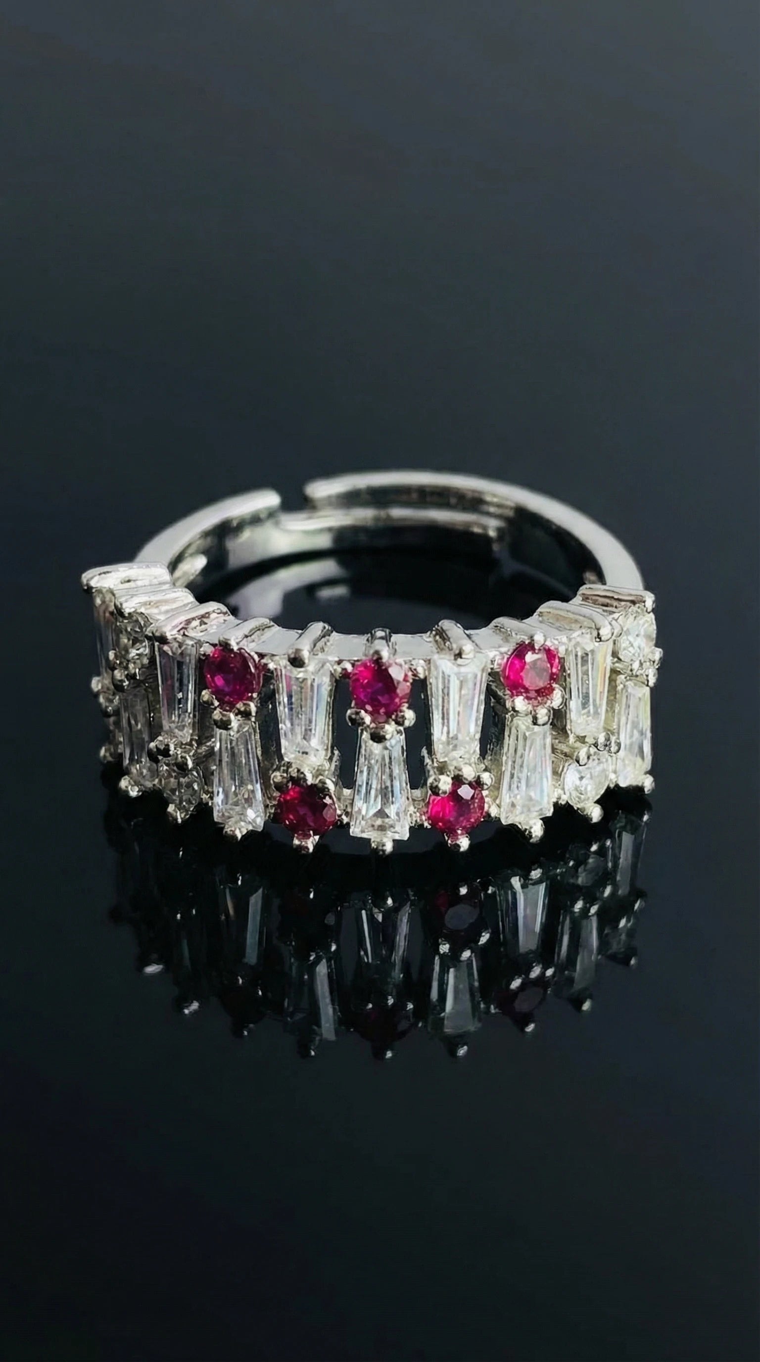 Silver ring alternating round red gemstones and tapered baguette clear stones set in a continuous band
