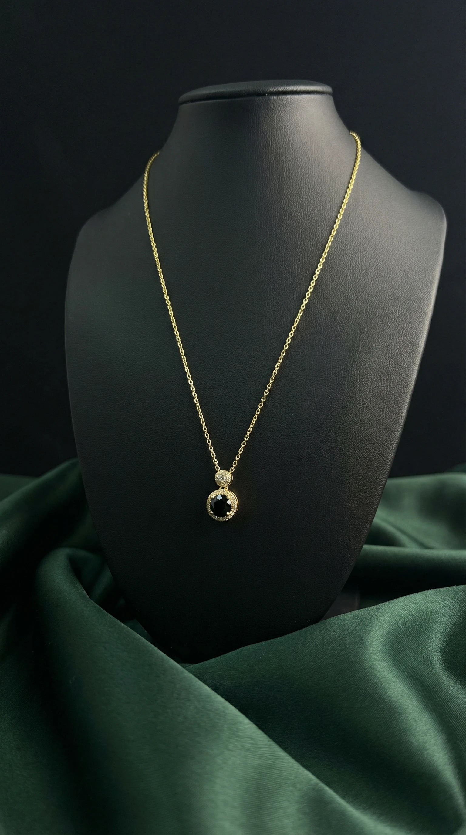 Gold necklace with a black pendant on a black mannequin against a dark green fabric background