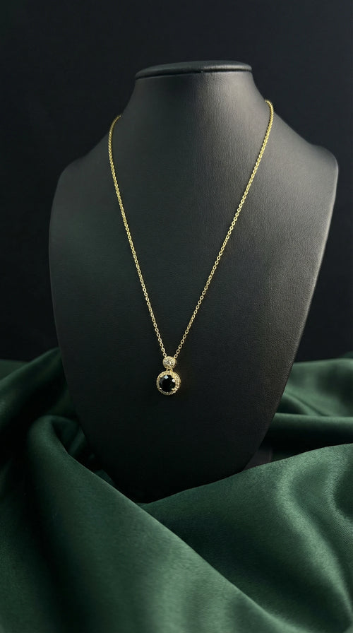 Gold necklace with a black pendant on a black mannequin against a dark green fabric background