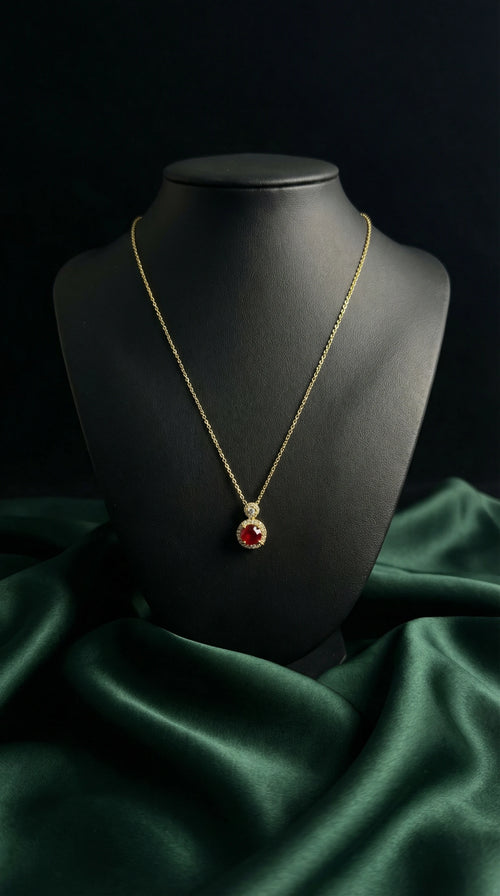 Gold necklace with a red pendant on a black mannequin bust against a dark background