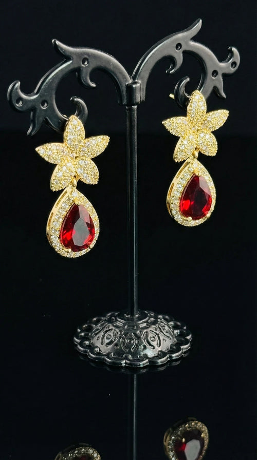 Gold floral-shaped earrings with small clear gemstones and a large teardrop-shaped red gemstone pendant.