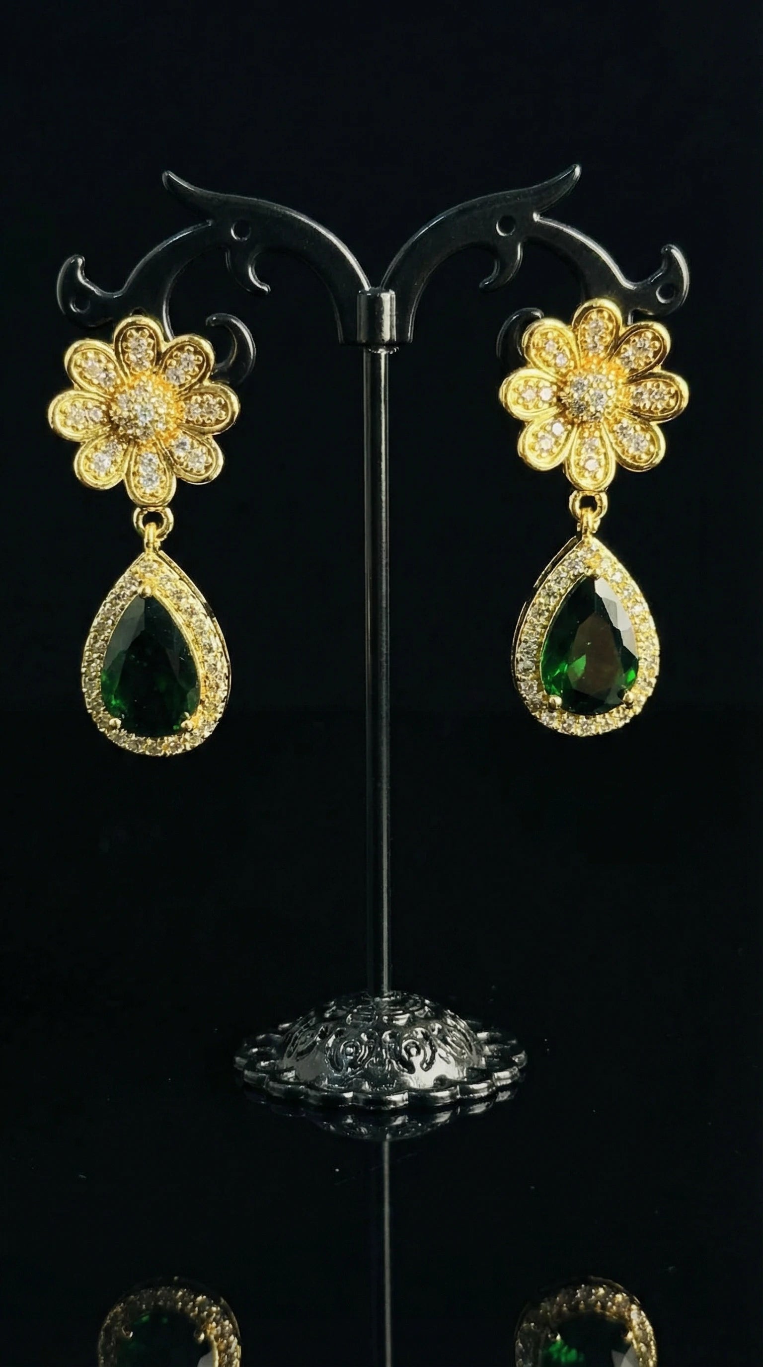 Gold flower-shaped earrings with clear gemstones and large teardrop-shaped green gemstones surrounded by small clear stones.